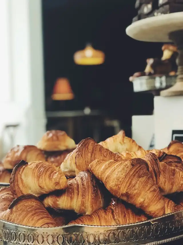 Croissants dourados empilhados numa bandeja metálica trabalhada, com o fundo desfocado.
